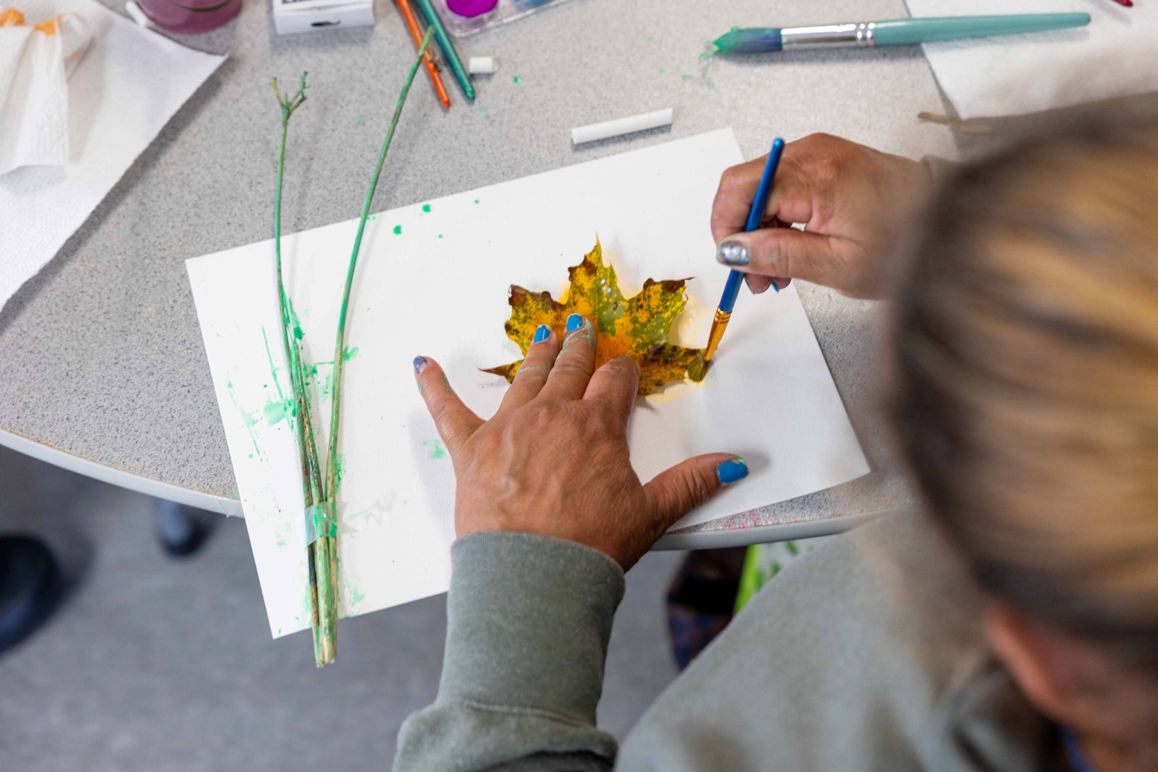 Photo of a woman's hand while she traces a leaf as she creates a watercolor painting.