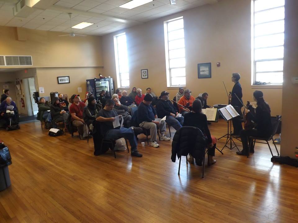 Three women playing violins for an audience of Lifebridge clients.