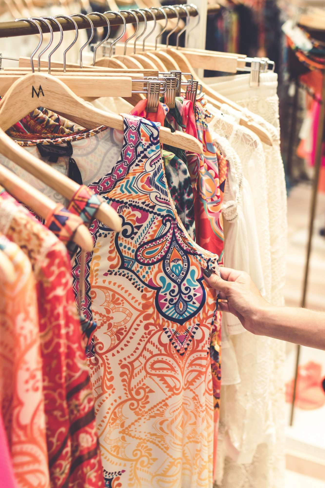 A hand pulling out a dress from a rack to get a better look.