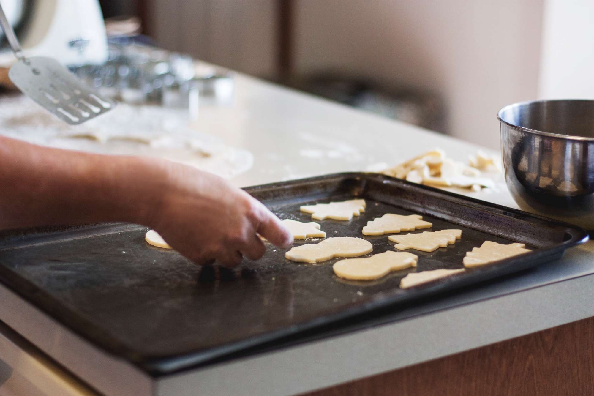 A hand places cut-outs of cookie dough on a baking sheet.