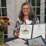 Honoree Karen Andrew smiles and holds proclamations from the U.S. and local governments at Breaking Bread, Building Hope