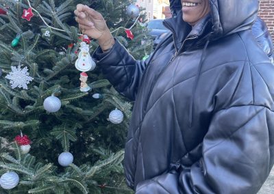 Woman smiling holding up snowman ornament in front of the Christmas tree