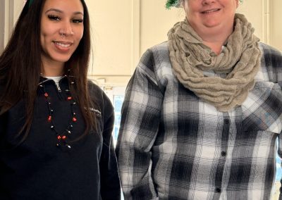 Two women smiling, one with reindeer antlers and the other with a Christmas tree hat